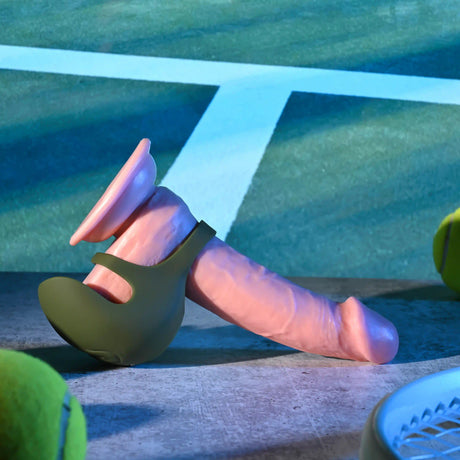 Zero Tolerance Nutty Buddy Vibrating Cock Ring Green on a surface with tennis equipment in the background.