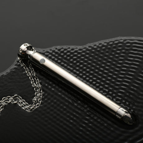 Charmed 7X Vibrating Necklace Silver on a textured surface showcasing its sleek design and chain.