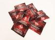 ID Studded Condoms 144 Count Bag displayed in a dynamic pile, showcasing vibrant foil packaging.
