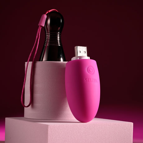 Selopa Companion Rechargeable Silicone Egg Pink resting next to a chrome handle and a USB connector, featuring vibrant colors.