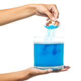 A hand adding blue Kama Sutra Treasures Of The Sea Bath Salt to a glass filled with tropical ocean water.