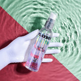 Playboy Pleasure Slick Silicone Lubricant 4 Oz bottle in a hand with water droplets on a colorful background.