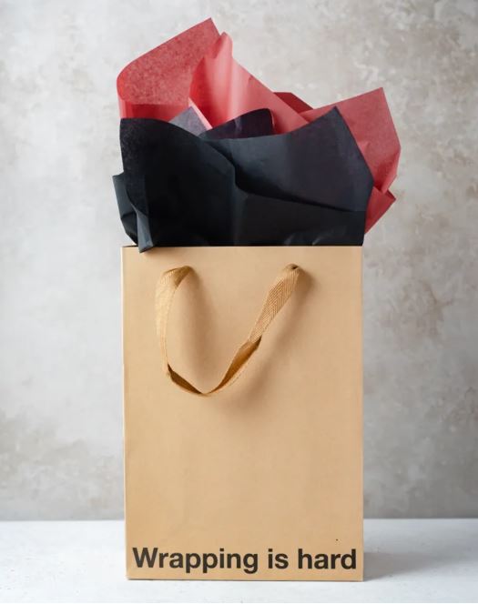 Wood Rocket Wrappin Is Hard Gag Gift Bag with colorful tissue paper on top.